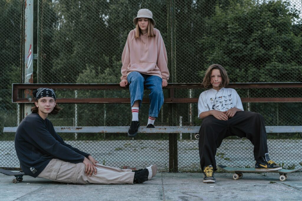 Tre unge tenåringer, jente i midten og gutter på hver side, sitter på og rundt en bank, henslengt i parken