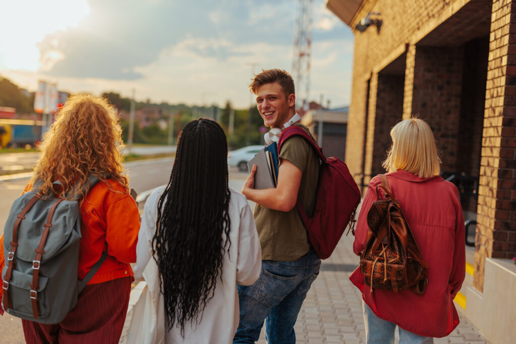 En gruppe ulike universitetsstudenter går på campus. En mannlig student snur seg og ser mot kameraet over skulderen og smiler.